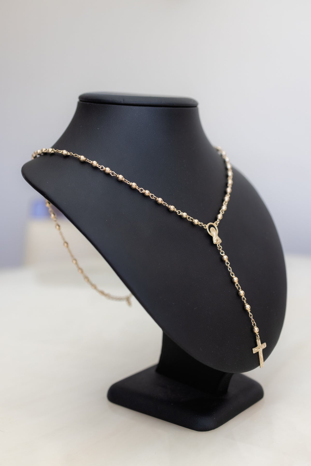 Three-quarter view of the handmade 9ct gold rosary necklace on a display bust