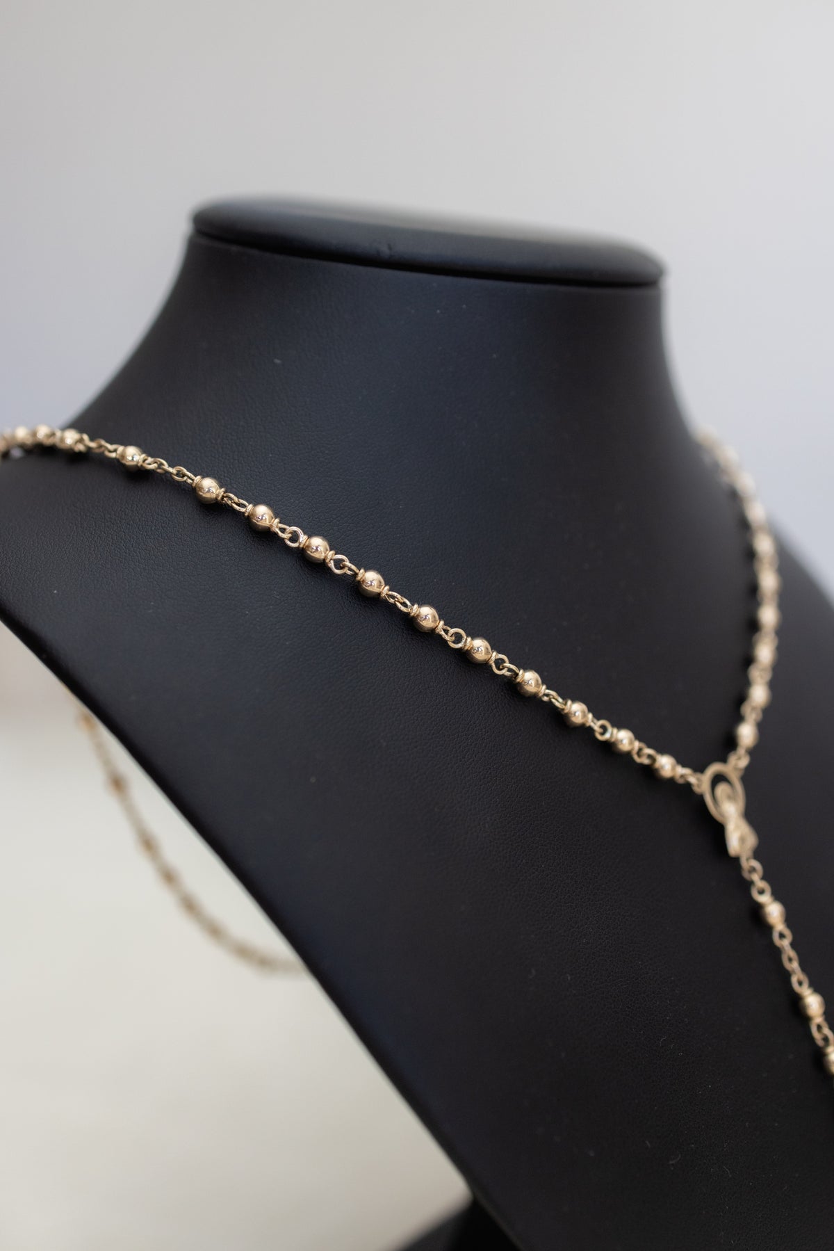 The 4mm gold beads of the rosary necklace running across a black display bust
