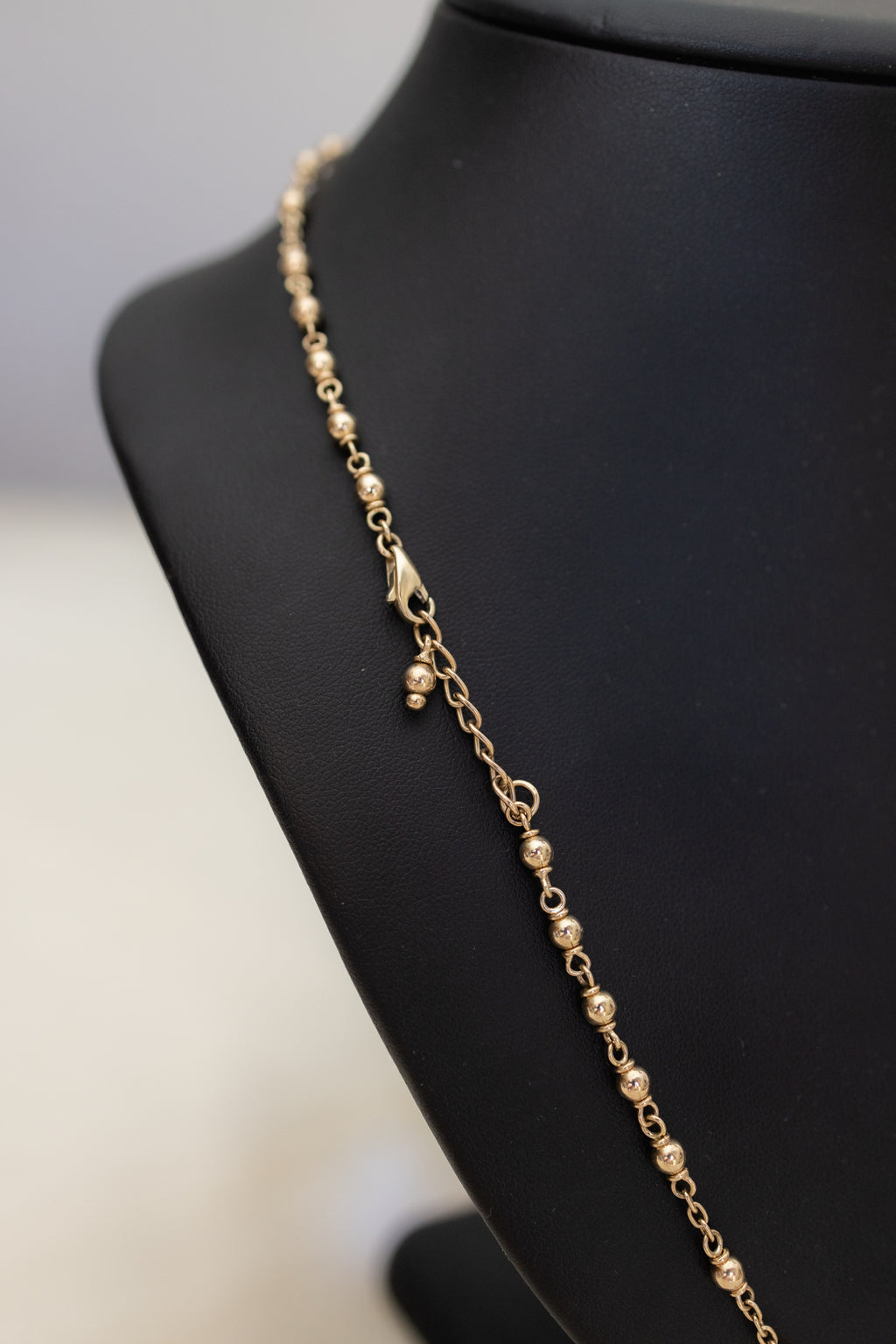 Gold bead and clasp detail on the 9ct gold rosary necklace against a black bust