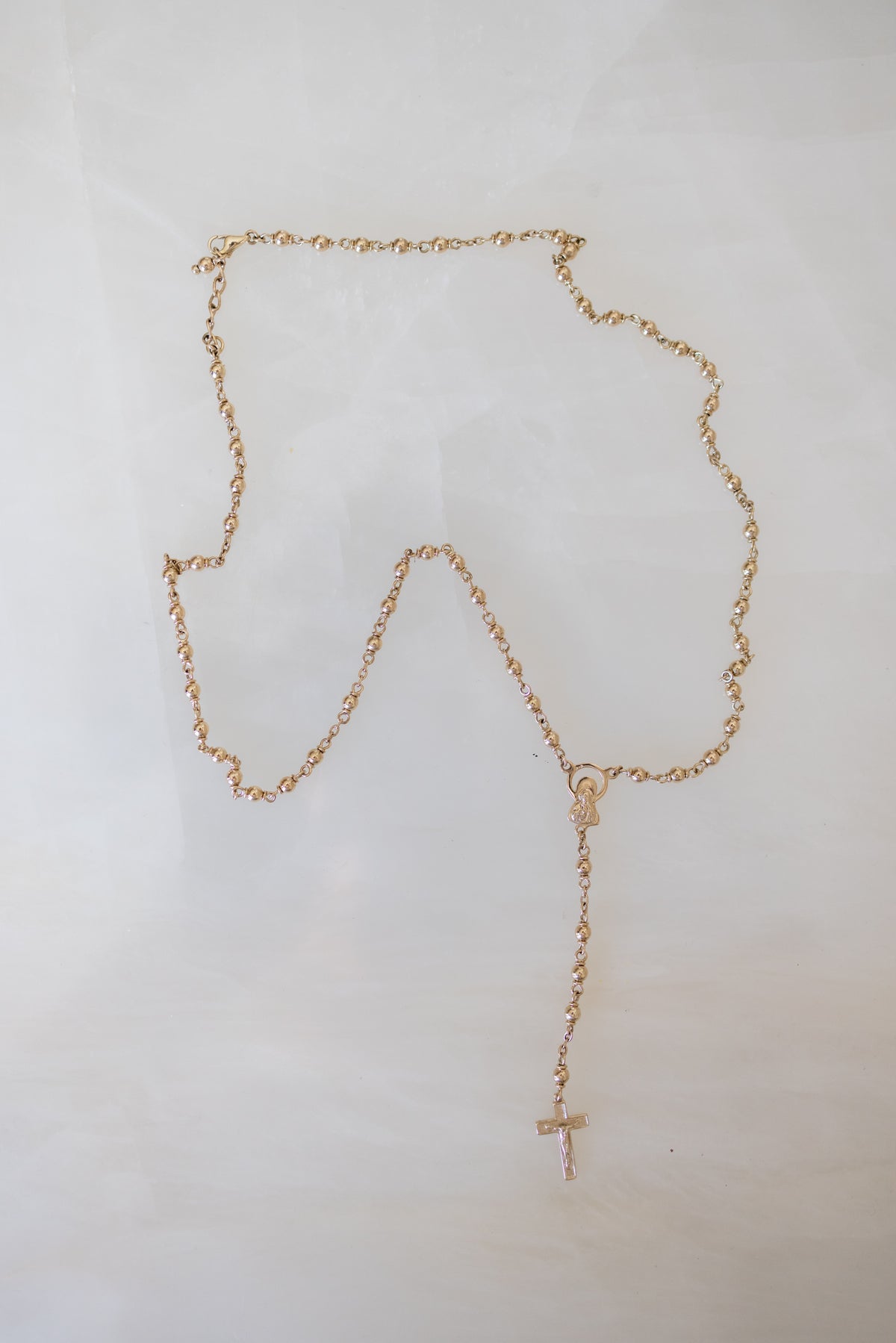The complete 9ct gold rosary necklace laid flat on a white background