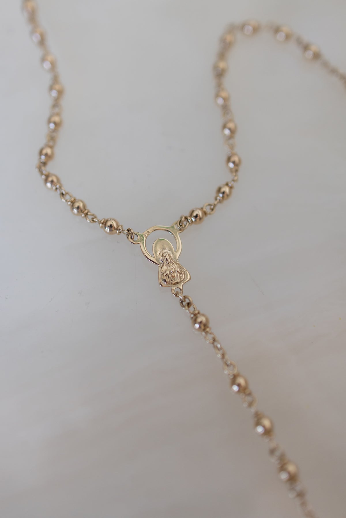 Flat lay detail of the Marian centrepiece and 4mm gold beads of the rosary
