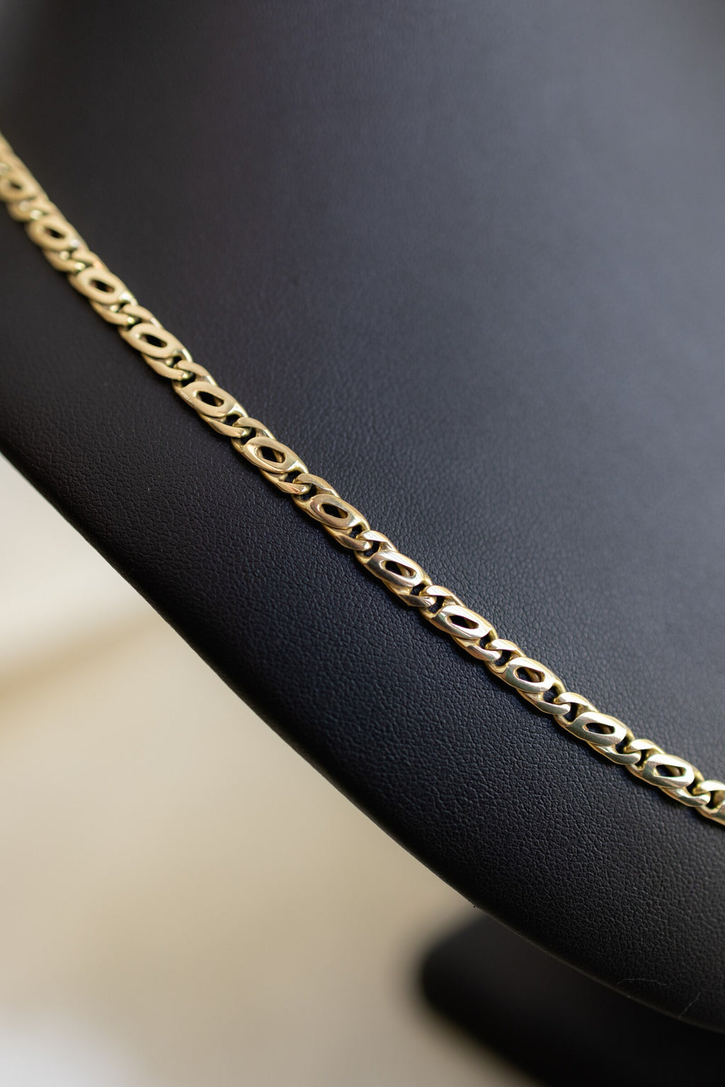 Detail of the 4.5mm handmade birdseye link chain in 9ct gold lying flat on a black bust