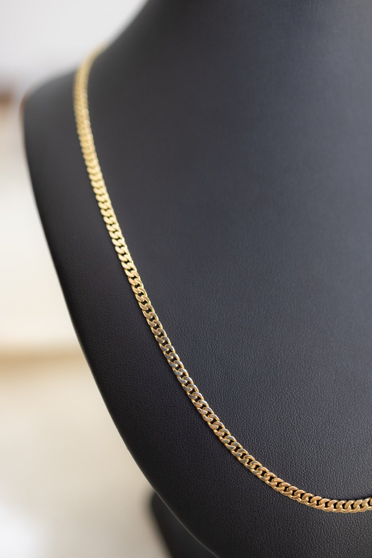 3.3mm 9ct yellow gold Cuban link chain curving over the shoulder of a display bust