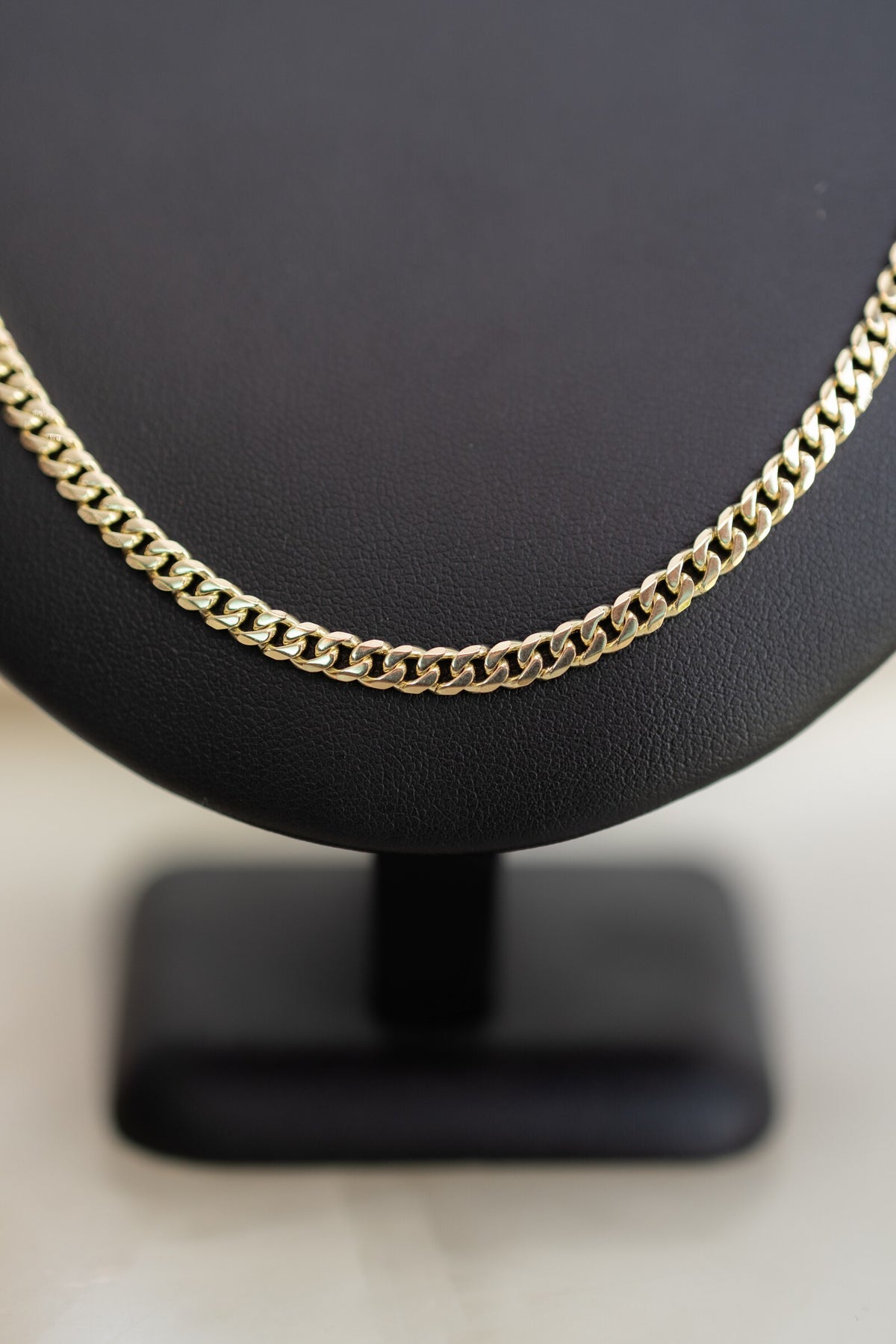Close view of the 4.1mm handmade 9ct yellow gold Cuban link chain across a black bust