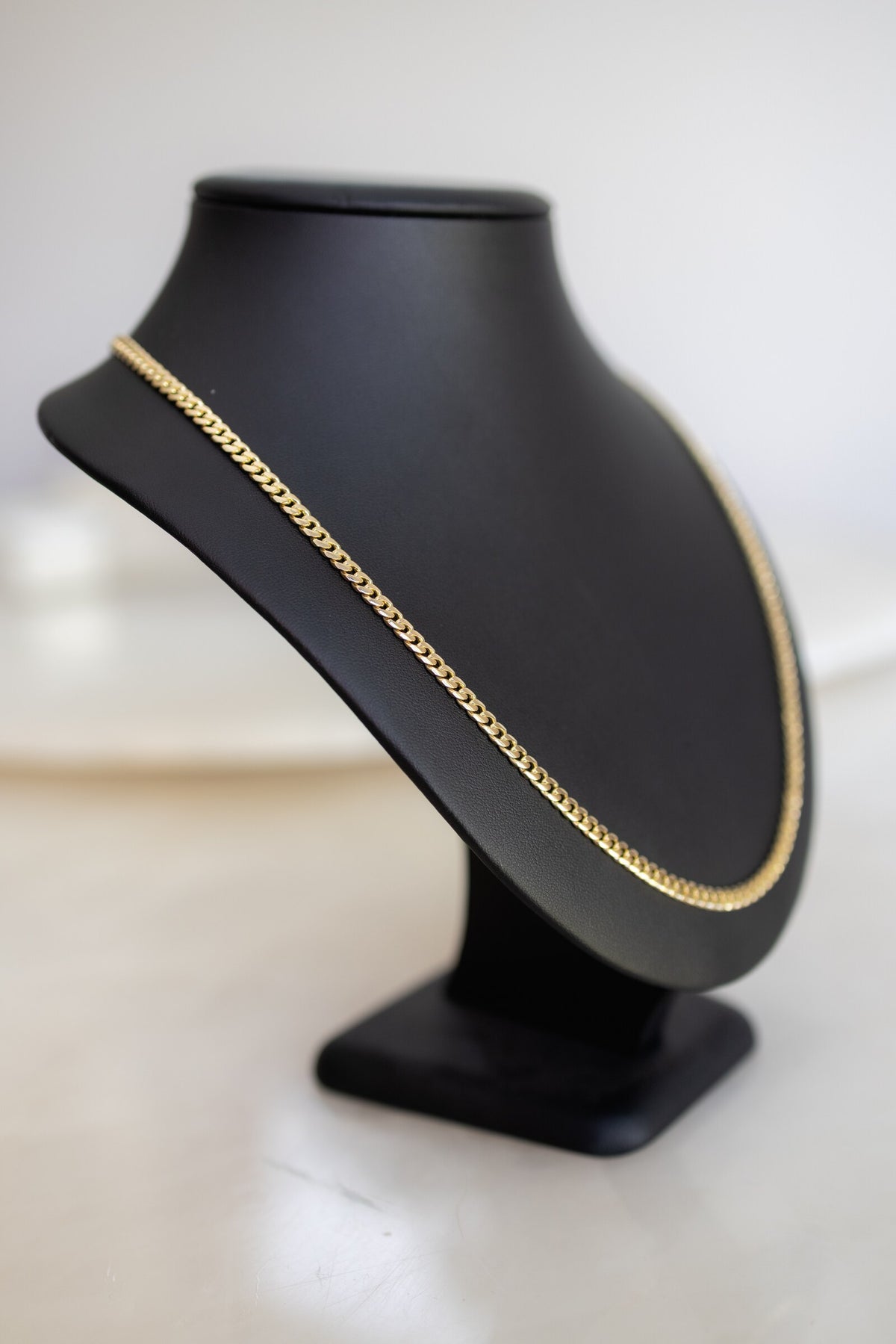4.4mm handmade 9ct yellow gold Cuban link chain seen from the side on a display bust