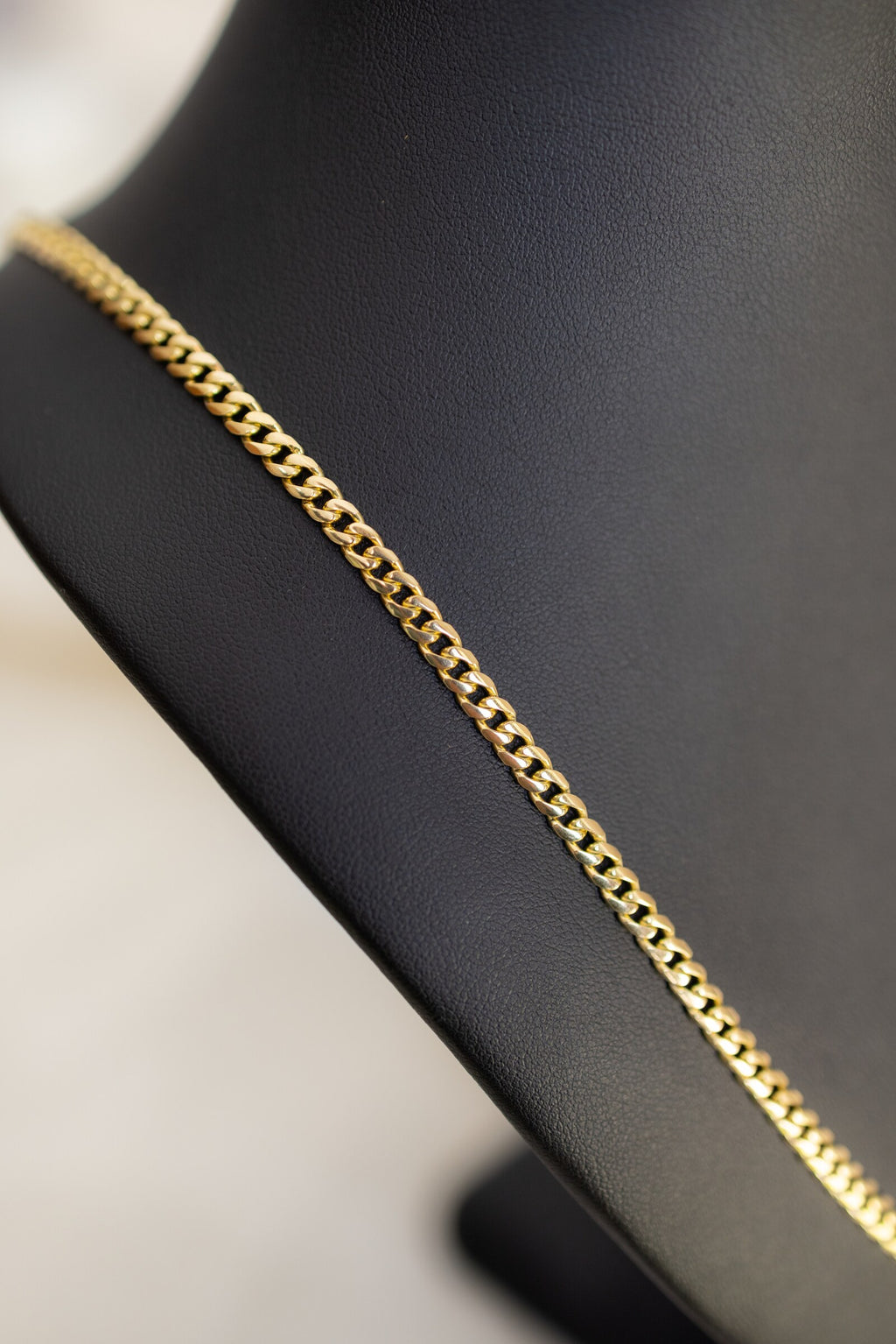 Close view of the 4mm handmade 9ct gold Cuban link chain running across a black bust